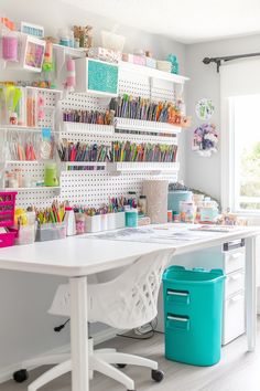 a white desk topped with lots of crafting supplies next to a wall filled with shelves