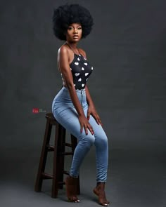 a woman sitting on top of a wooden stool wearing jeans and a polka dot shirt