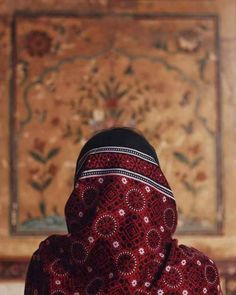 a woman wearing a red and black shawl standing in front of a wall painting