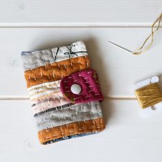 an orange, white and pink cell phone case next to a spool of thread