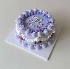 a birthday cake with purple frosting and decorations on it's side, sitting on top of a white surface