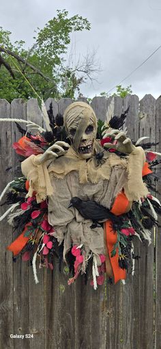 a creepy scarecrow hanging on a wooden fence with flowers and feathers around it's neck