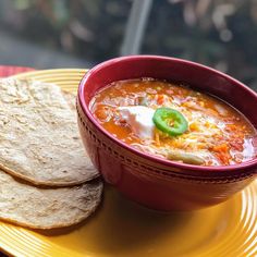 a red bowl filled with soup next to two tortillas on a yellow plate