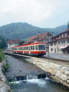 a red and white train traveling down tracks next to houses on the side of a river