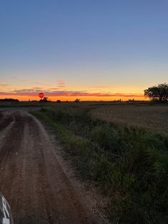 the sun is setting over a dirt road