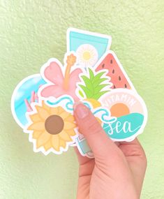 a hand holding up a sticker that says sea with flowers and sunflowers