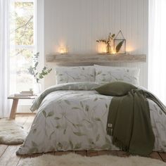 a bed with white sheets and green leaves on it in front of a window filled with candles