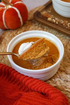 a bowl of pumpkin soup with a spoon in it and two pumpkins on the side