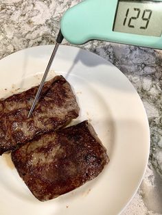 two pieces of steak on a plate with a thermometer in front of it