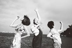 three women standing next to each other in front of the ocean with their hands up