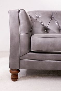 a gray leather chair with wooden legs and buttons on the arm rests against a white wall