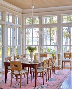 a dining room table with chairs and a rug in front of large windows that overlook the water