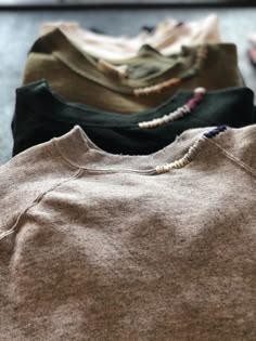 four different colored sweaters are lined up on the floor, with beads hanging from them