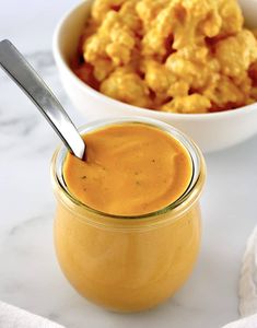 a bowl of macaroni and cheese next to a jar of orange colored sauce