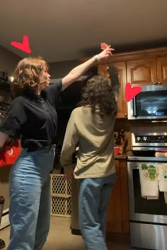 two women are dancing in the kitchen with red paper hearts on their backs and arms