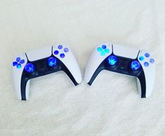 two video game controllers sitting side by side on a bed with white sheets and blue flowers