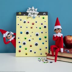 two elfs are sitting next to an apple and a bulletin board with magnets on it