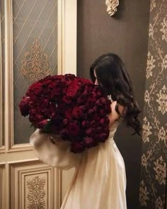 a woman in a white dress holding a large bouquet of red roses while standing next to a mirror