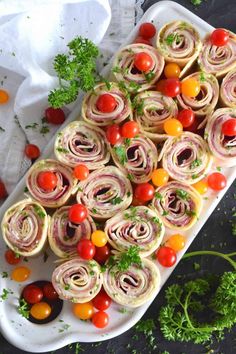 a platter filled with rolled up veggies and tomatoes