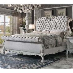 a white bed sitting in a bedroom on top of a blue rug and a chandelier