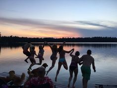 people jumping into the water at sunset on a dock with their arms in the air