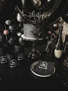 a table topped with black and silver balloons, cake and confetti cups next to each other