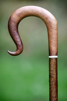 an old wooden walking stick with a curved handle on it's end, in front of a blurred green background