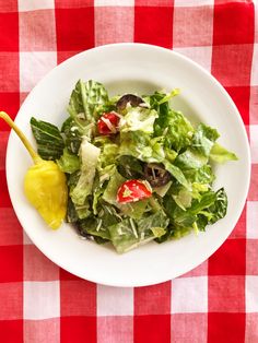 a white bowl filled with salad on top of a red and white checkered table cloth