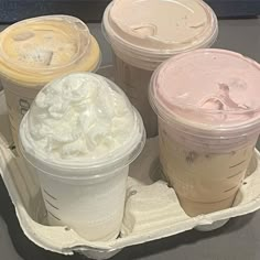 four different types of drinks in plastic cups on a tray with ice cream and whipped cream