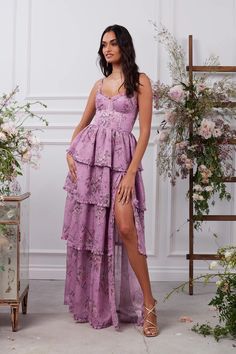 a woman wearing a purple dress standing in front of a floral display with flowers and greenery