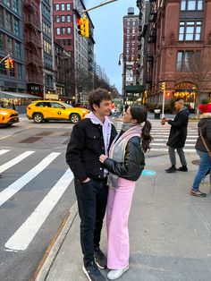 a man and woman standing next to each other on a street corner in the city