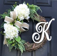 a monogrammed wreath with white flowers and greenery hangs on the front door