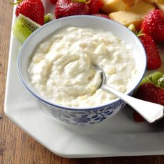 a bowl of yogurt with strawberries on the side and sliced apples in the background