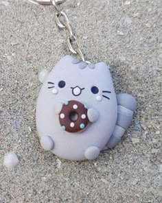 a cat keychain with a donut in it's mouth on the sand