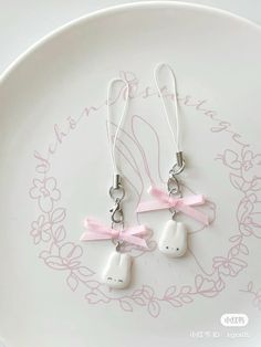 two cute little white bunny earrings with pink bows hanging from the ear wires on a plate