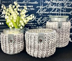 three crocheted jars with labels on them sitting next to a vase filled with flowers