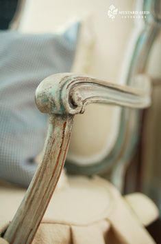 an old wooden chair with peeling paint on the armrests and back end, in front of a blue pillow