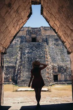 a woman in a dress and hat walks through an archway to the ruins at chichena