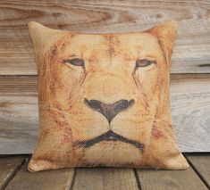 a pillow with a lion's face painted on the front and side, sitting on a wooden floor