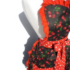 a woman's apron with red cherries and polka dots on it, sitting on a mannequin