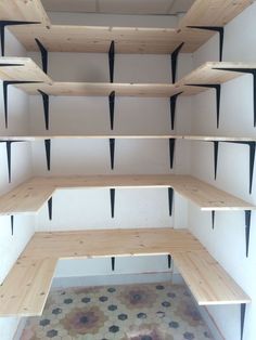 an empty room with several shelves and black metal brackets on the wall, in front of a tiled floor