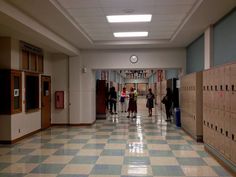 several people are walking down the hallway in an empty building with lockers on both sides