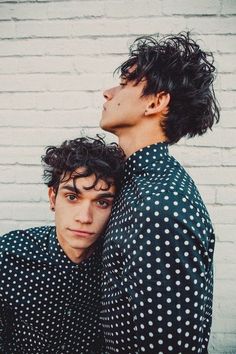 two young men standing next to each other in front of a white brick wall with black and white polka dots