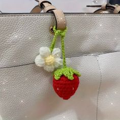 a crocheted strawberry hanging from a white purse with a flower attached to it