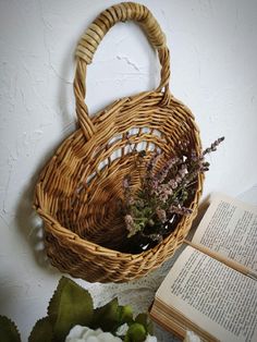 a wicker basket with flowers in it next to an open book