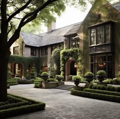 a large house with lots of trees and bushes in front of it on a brick walkway