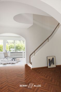 an empty room with wooden flooring and white walls, along with a staircase leading up to the second floor