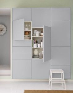 a white chair sitting in front of a gray cabinet with shelves and dishes on it