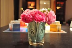 pink flowers are in a glass vase on a table with money notes and cash bills