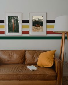 a brown leather couch sitting in front of two pictures on the wall above it and a lamp next to it